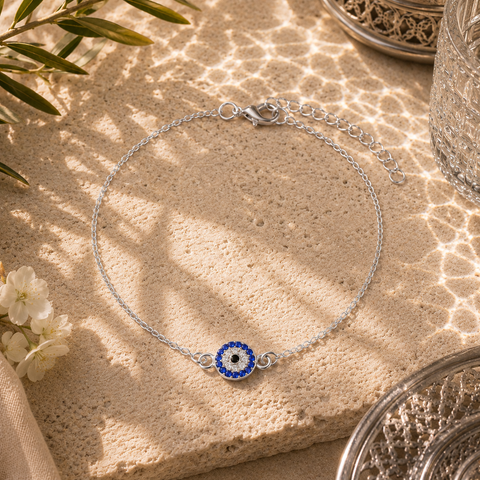 Elegante Safira Fußkette in Silber mit funkelndem Nazar Auge als traditionellem Schutzsymbol und Glücksbringer. Hochwertig inszeniert auf feinem Sand mit mediterranen Lichtreflexionen, silbernen Ornamenten und sommerlicher Atmosphäre. Filigraner Schmuck für stilvolle Alltagslooks, Urlaub und besondere Anlässe.