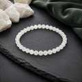 São Paulo Weiß-Jade-Armband mit 6 mm großen, leicht transparenten weißen Perlen auf dunklem Schiefer, umgeben von hellen Natursteinen und dunkelgrünem Stoff.
