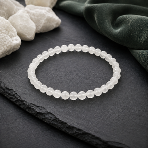 São Paulo Weiß-Jade-Armband mit 6 mm großen, leicht transparenten weißen Perlen auf dunklem Schiefer, umgeben von hellen Natursteinen und dunkelgrünem Stoff.