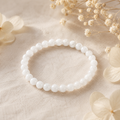 Filigranes Solid White Jade Natursteinarmband mit 6 mm großen, leicht transparenten weißen Perlen auf hellem Leinen mit dezenten weißen Trockenblumen.