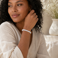 Frau trägt das Solid White Jade Natursteinarmband mit 8 mm großen weißen Perlen am Handgelenk in einer hellen, natürlichen Umgebung mit cremefarbenen Stoffen und weißen Blumen.
