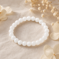 Solid White Jade Natursteinarmband mit 8 mm großen, sanft schimmernden weißen Perlen auf beigefarbenem Naturstoff mit hellen Blumen und filigranen Trockenblüten.