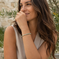 Frau trägt das Tree Agate Natursteinarmband mit 6 mm großen grün-creme gemusterten Perlen am Handgelenk in einer mediterranen Gartenkulisse mit Olivenzweigen.