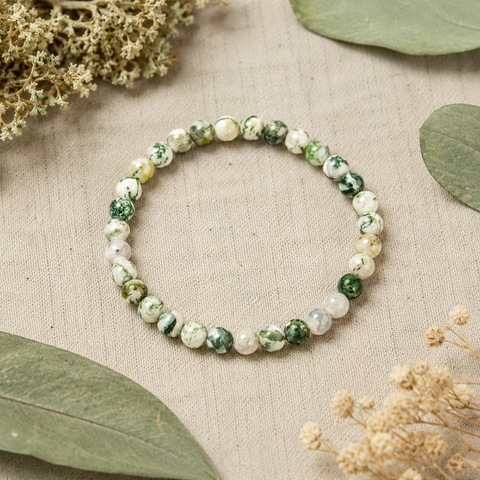 Tree Agate Natursteinarmband mit 6 mm großen, individuell gemusterten Perlen in Grün, Creme und Weiß auf hellem Leinen mit Eukalyptusblättern und dezenten Trockenblumen.