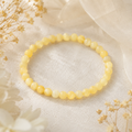 Yellow Calcite Jade Natursteinarmband mit 6 mm großen, leicht marmorierten Perlen in zarten Gelb- und Cremetönen auf hellem Stoff mit dezenten Trockenblumen präsentiert.