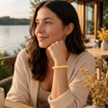 Frau trägt das Yellow Calcite Jade Natursteinarmband mit 8 mm großen gelben Perlen zu einem hellen Strickoutfit auf einer sonnigen Terrasse am See.