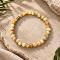 Gelbes Natursteinarmband mit 6-mm-Perlen in Creme-, Honig- und Goldtönen mit goldfarbenem Akzent auf hellem Naturstein.