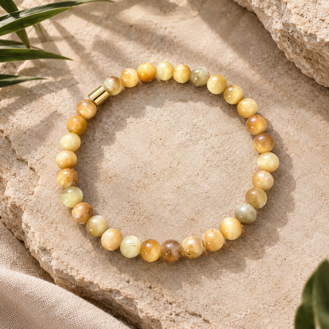 Gelbes Natursteinarmband mit 6-mm-Perlen in Creme-, Honig- und Goldtönen mit goldfarbenem Akzent auf hellem Naturstein.