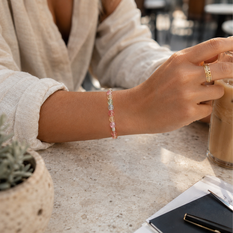 Frau trägt pastellfarbenes Kristallarmband mit facettierten 8-mm-Perlen am Handgelenk in einer natürlichen Café-Szene.