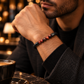 Mann trägt das ROAN Rotes Tigerauge Armband mit fünf rot gemaserten Tigerauge-Perlen und schwarzem geflochtenem Band.