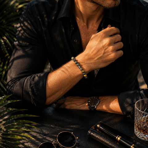 Ausschnitt eines Mannes in dunklem Hemd mit Tigerauge-Armband am Handgelenk in einer eleganten Business-Lifestyle-Szene mit dunklem Hintergrund und warmem Licht.
