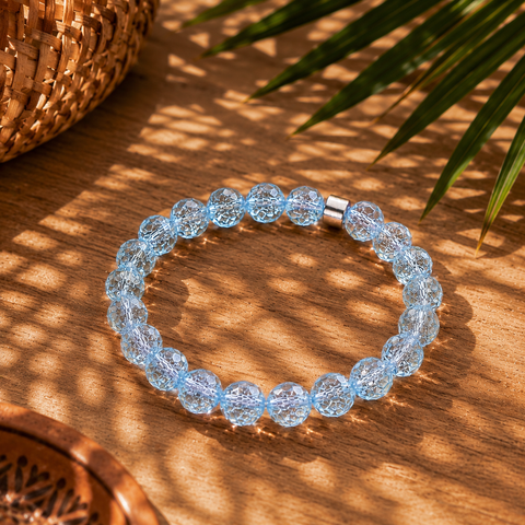 Hellblaues Bergkristall-Armband mit 8 mm großen Perlen im Diamantschliff auf warmem Holzuntergrund mit Palmenschatten und südamerikanisch inspirierten Naturdetails.