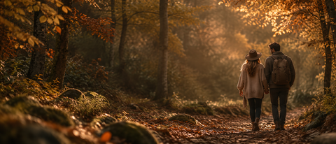 Paar bei einem herbstlichen Waldspaziergang auf einem goldenen Waldweg in warmer Abendstimmung.