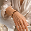 Frau trägt ein facettiertes Rauchquarz-Armband mit 8 mm großen braunen Perlen und goldfarbener Akzentperle am Handgelenk in heller, eleganter Umgebung.