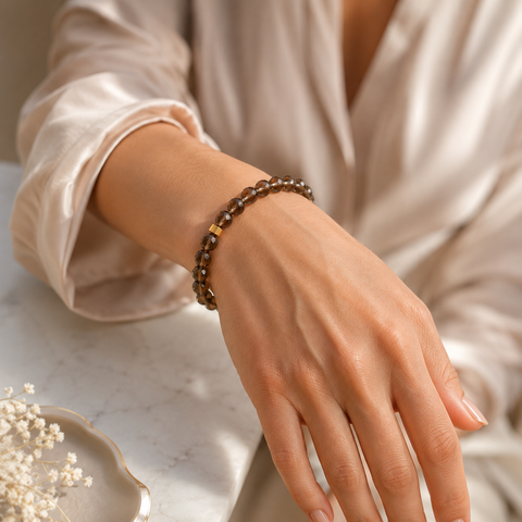Frau trägt ein facettiertes Rauchquarz-Armband mit 8 mm großen braunen Perlen und goldfarbener Akzentperle am Handgelenk in heller, eleganter Umgebung.